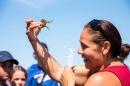 Woman in red shirt holds up a crab and smiles at it